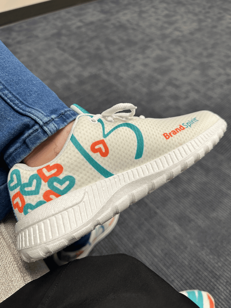 Custom promotional sneakers designed with Brand Spirit's signature teal and orange hearts for team uniforms.